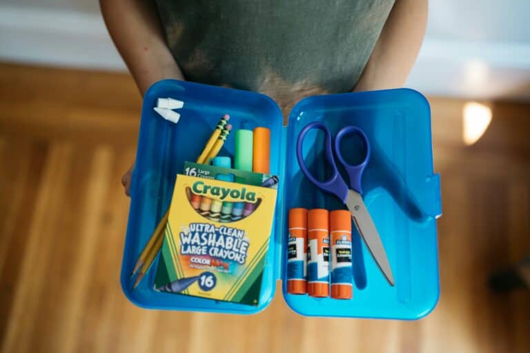 student holding school supplies that includes glue sticks, colored pencils, and highlighters